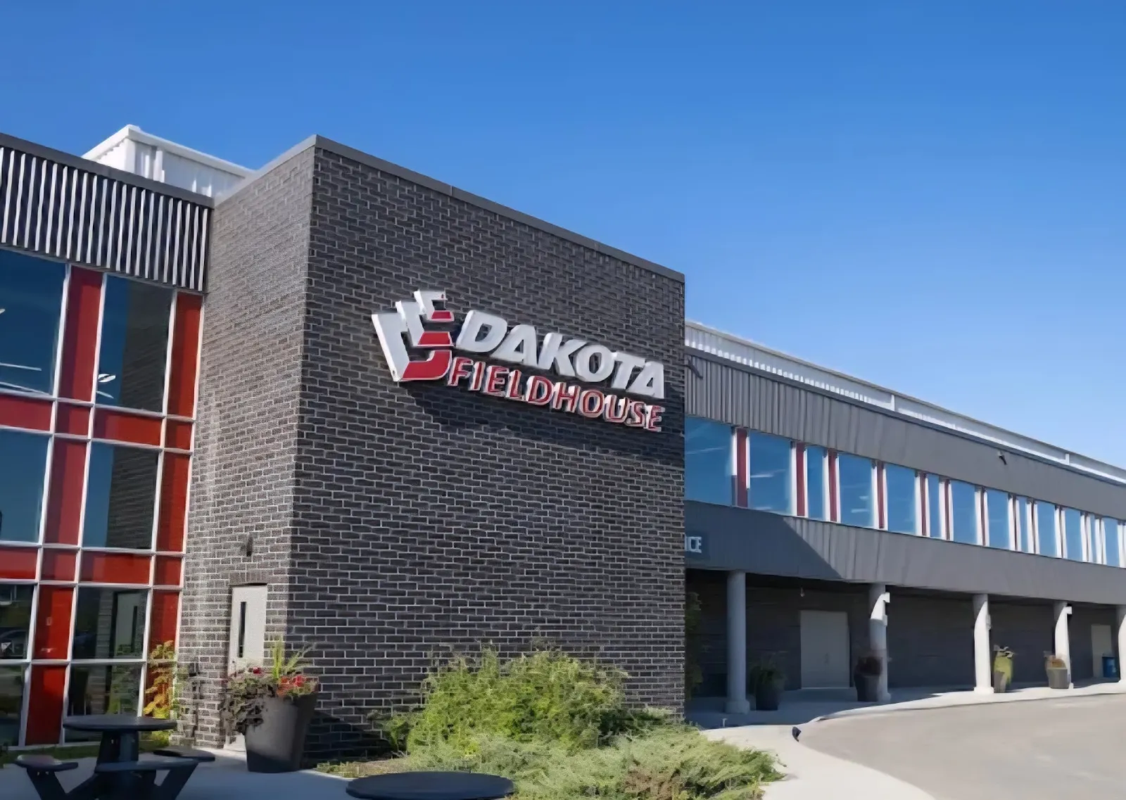The brick-and-glass Dakota Fieldhouse wing of the Dakota Community Centre complex on Dakota Street, under a clear blue sky. — Jonathan Toews Sportsplex