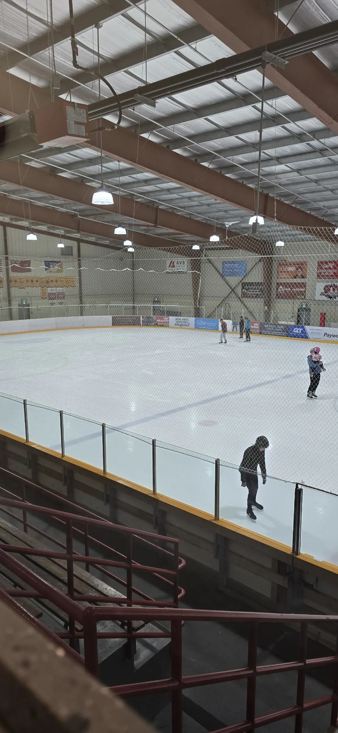 A quiet public skate at the Jonathan Toews Sportsplex, a few skaters on a wide sheet of ice under steel roof beams. — Jonathan Toews Sportsplex