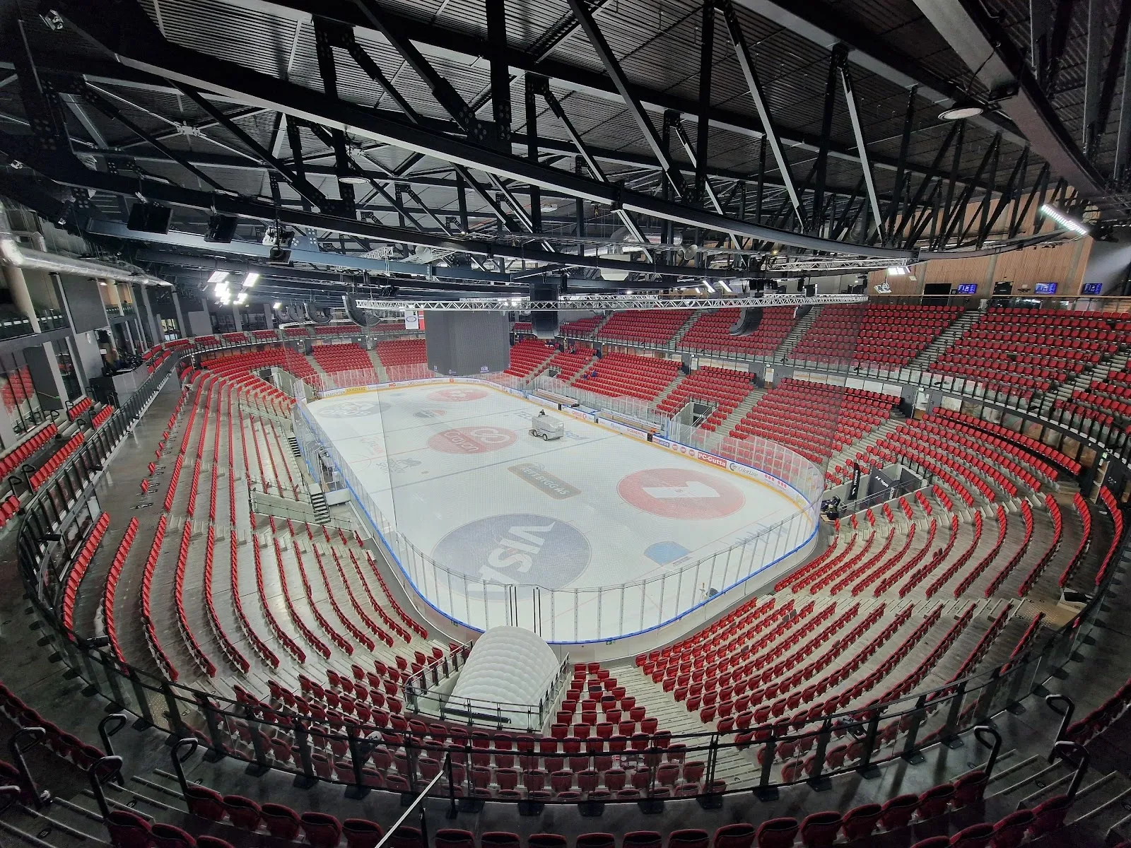 Isflaten i Jordal Amfi sett fra de øvre tribunene, med de røde tribunerekkene som svinger rundt isen og takkonstruksjonen over. — Jordal ungdomshall