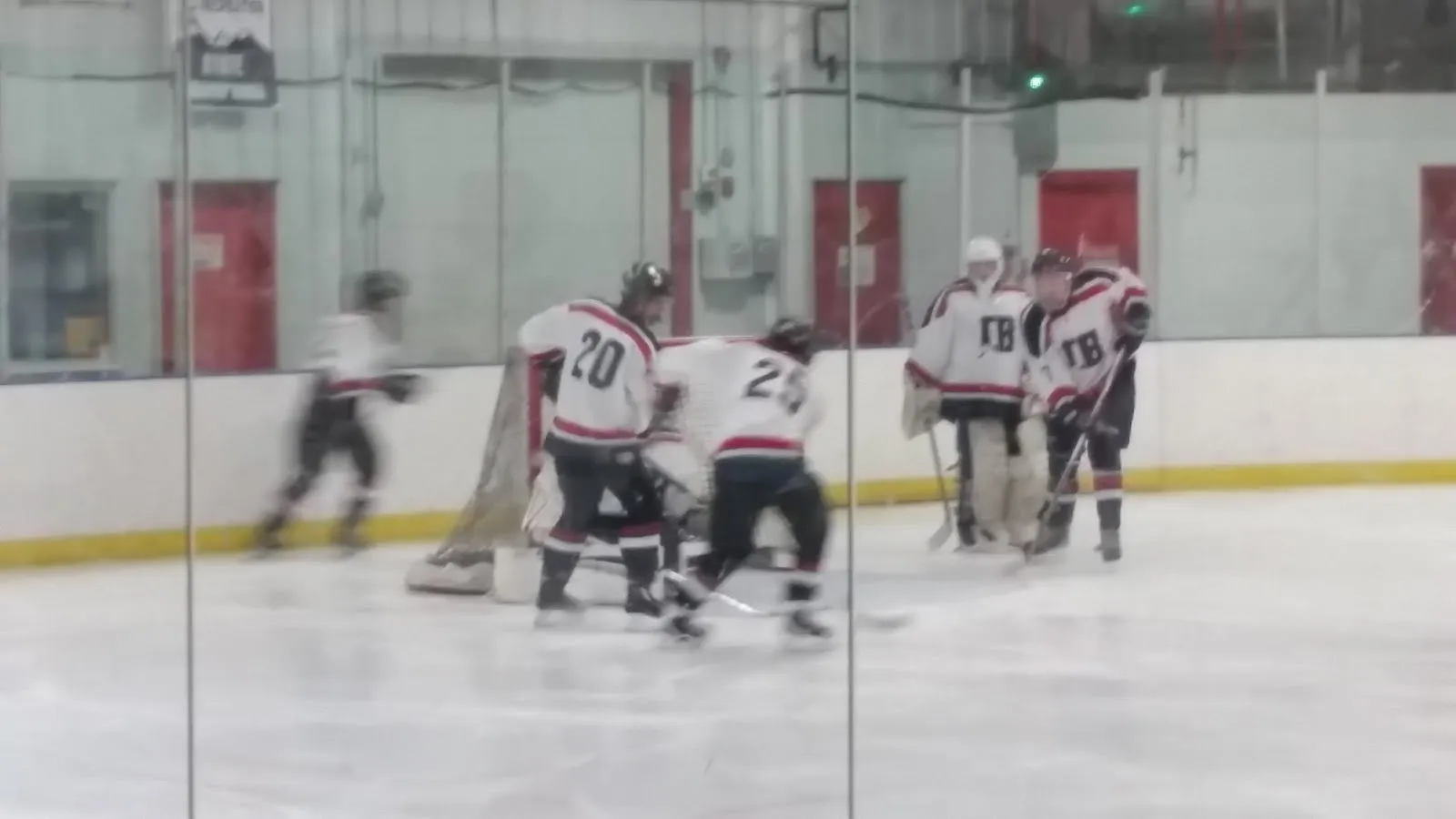 Un partido de hockey en la pista techada, con jugadores con jerseys blancos y negros alrededor de la portería, vistos a través del vidrio. — Jorgensen Ice Rink & Event Center