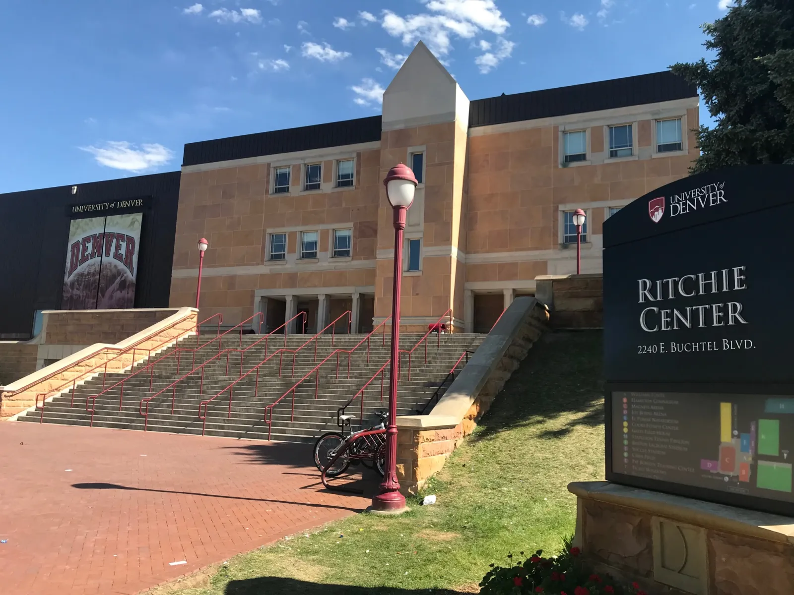 The Ritchie Center's brick and sandstone entrance front with its wide steps, the Denver banner on the wall and the sign giving 2240 E. Buchtel Blvd. — Joy Burns Arena