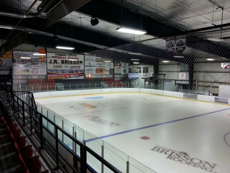 El hielo vacío desde las gradas, con el logo de Brisson pintado en el centro y anuncios de patrocinadores a lo largo del muro del fondo. — J.R. Brisson Complex (Casselman)