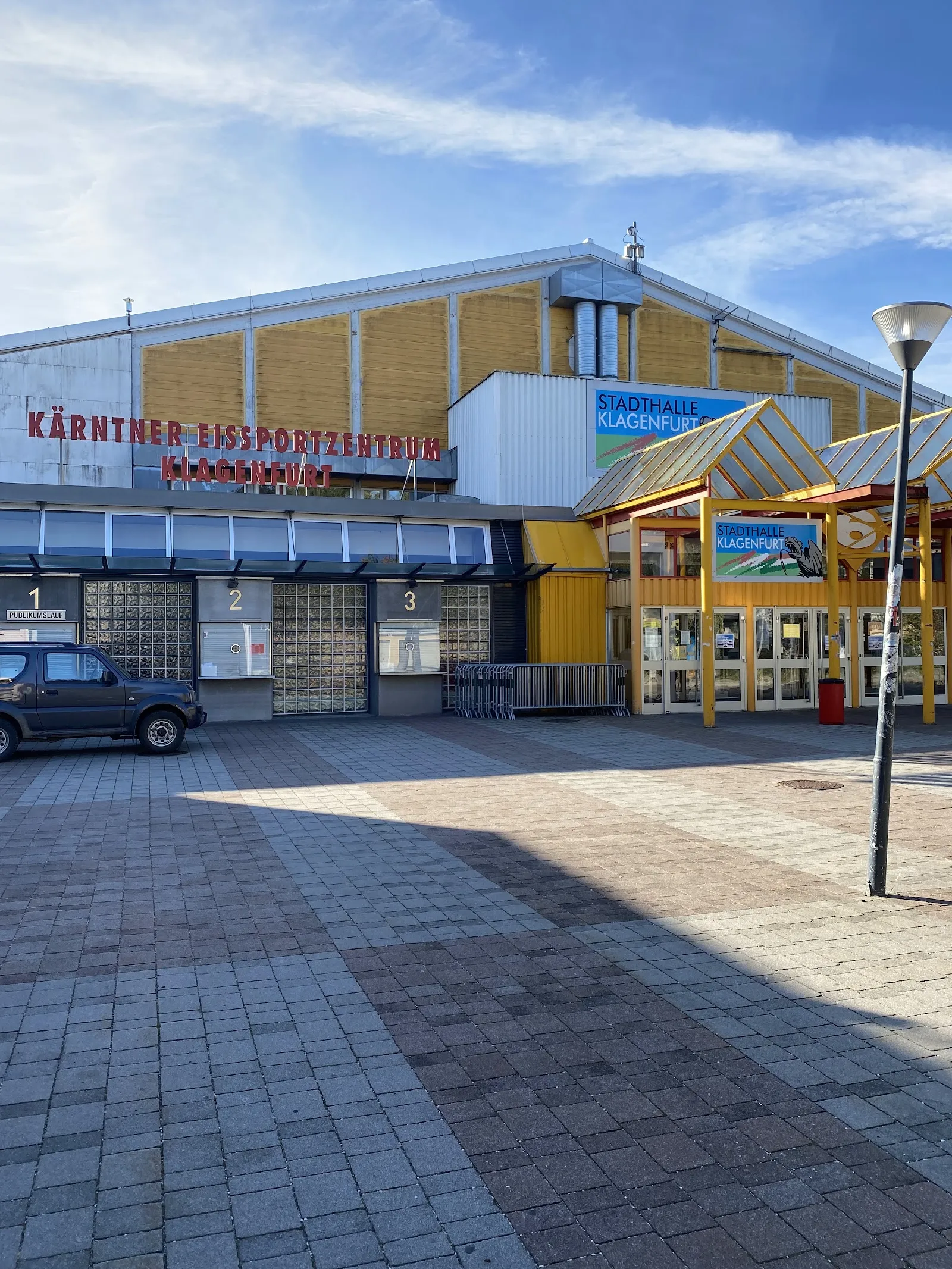 Die Eingangsfront des Kärntner Eissportzentrums in Klagenfurt mit dem Namensschild über den Glastüren und einer gelben Halle in Holzbauweise dahinter (Maps-Eintrag: Heidi Horten-Arena) – Kärntner Eissportzentrum Klagenfurt
