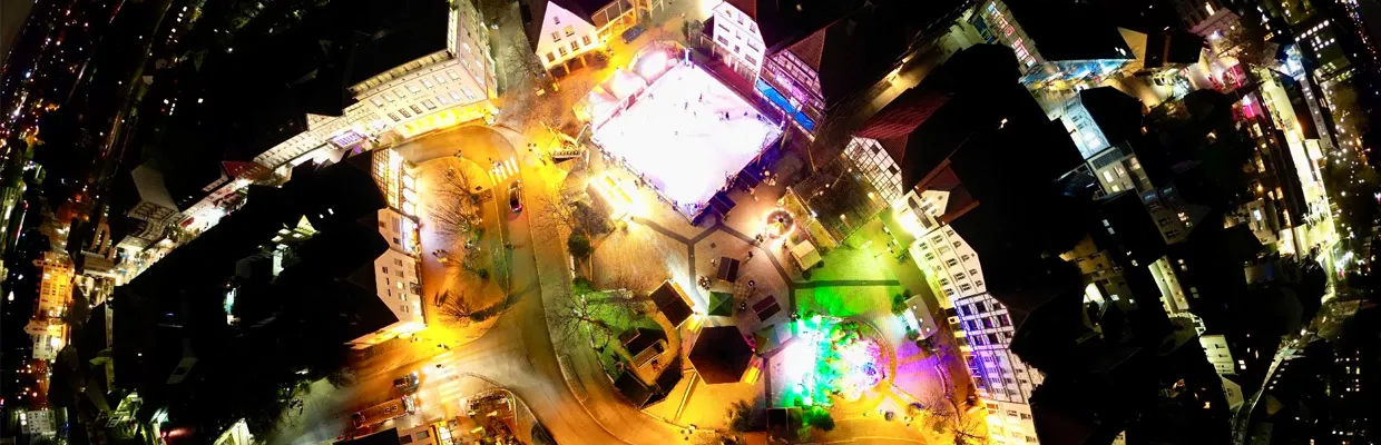 Nächtliche Luftaufnahme der Kamener Altstadt mit der hell erleuchteten Eisbahn auf dem Markt zwischen Giebelhäusern und Marktständen. – Eisbahn Kamener Winterwelt