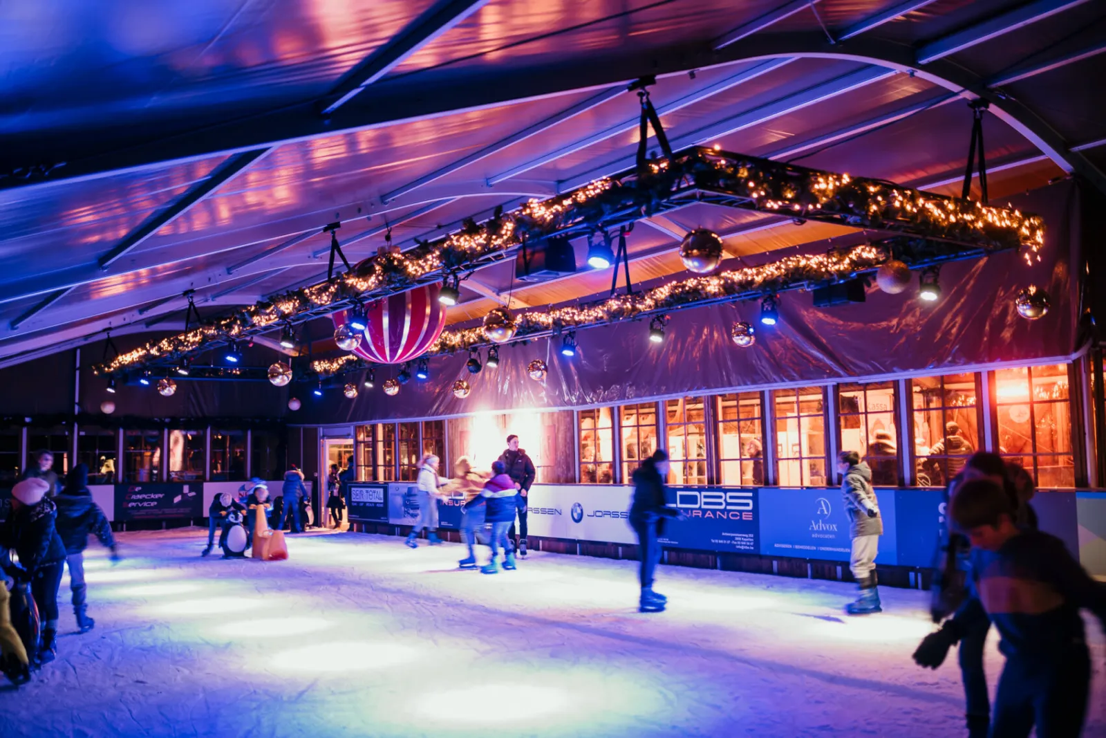 Skaters on the roofed Kapalpen rink at night, under garlands and spotlights, with a few skaters blurred in motion. — Kapalpen Kapellen