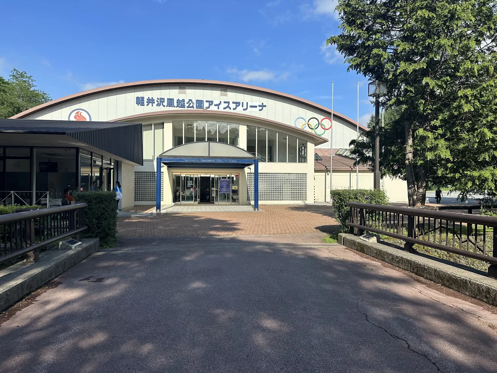 The entrance of the Karuizawa Kazakoshi Park Ice Arena, with the arena name over the door and the Olympic rings on the curved front — Karuizawa Kazakoshi Park Ice Arena