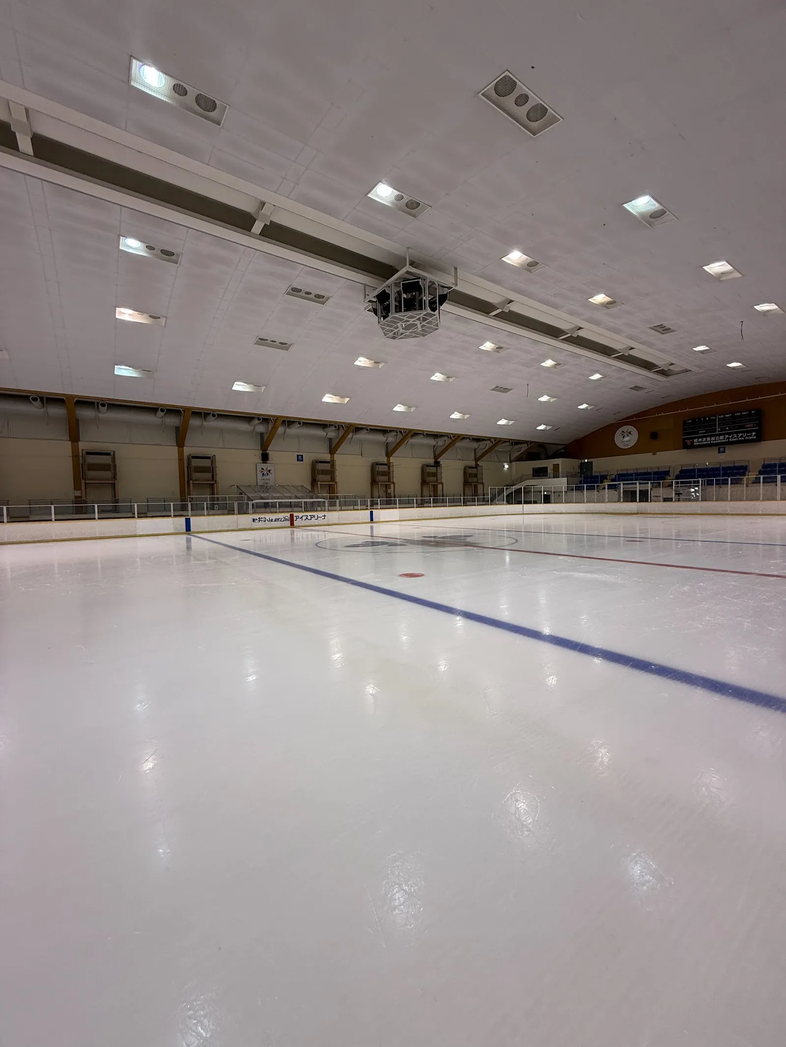 The empty ice sheet of the Karuizawa Kazakoshi Park Ice Arena seen from the rink side, with the boards and stands beyond — Karuizawa Kazakoshi Park Ice Arena
