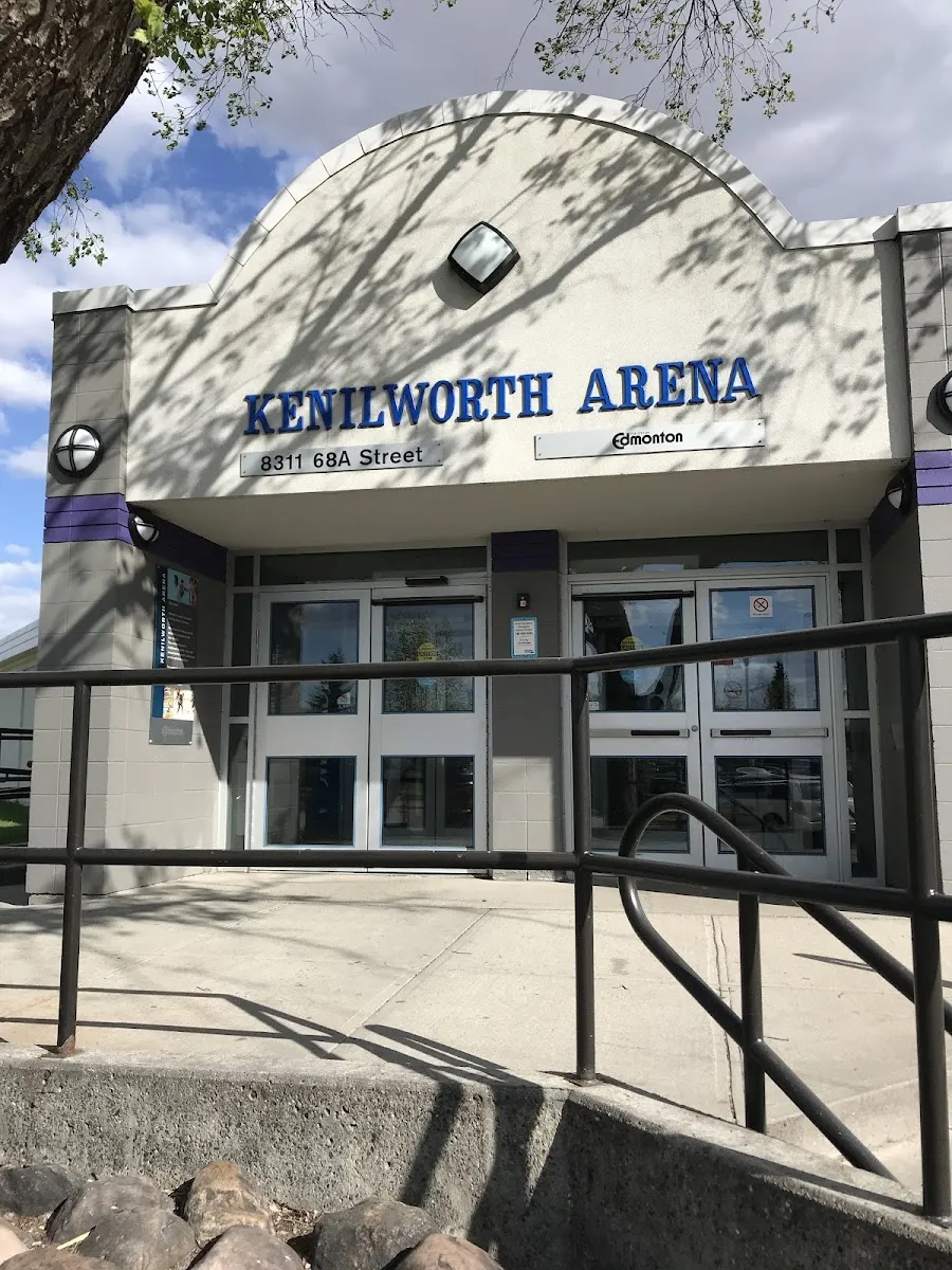 The arched front entrance of Kenilworth Arena in sunshine, with the name on the curved facade above the glass double doors and a railed ramp leading up to them. — Kenilworth Arena