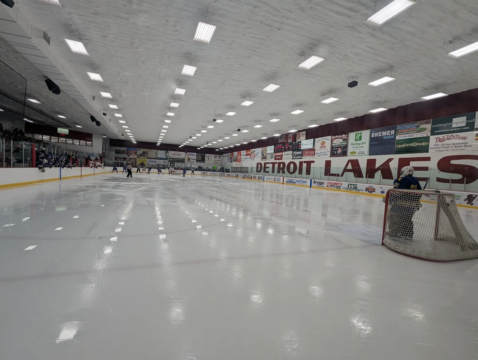 Una vista larga a lo largo de una pista vacía con el nombre Detroit Lakes en letras grandes sobre las vallas rojas bajo un techo claro de luces. — Kent Freeman Arena
