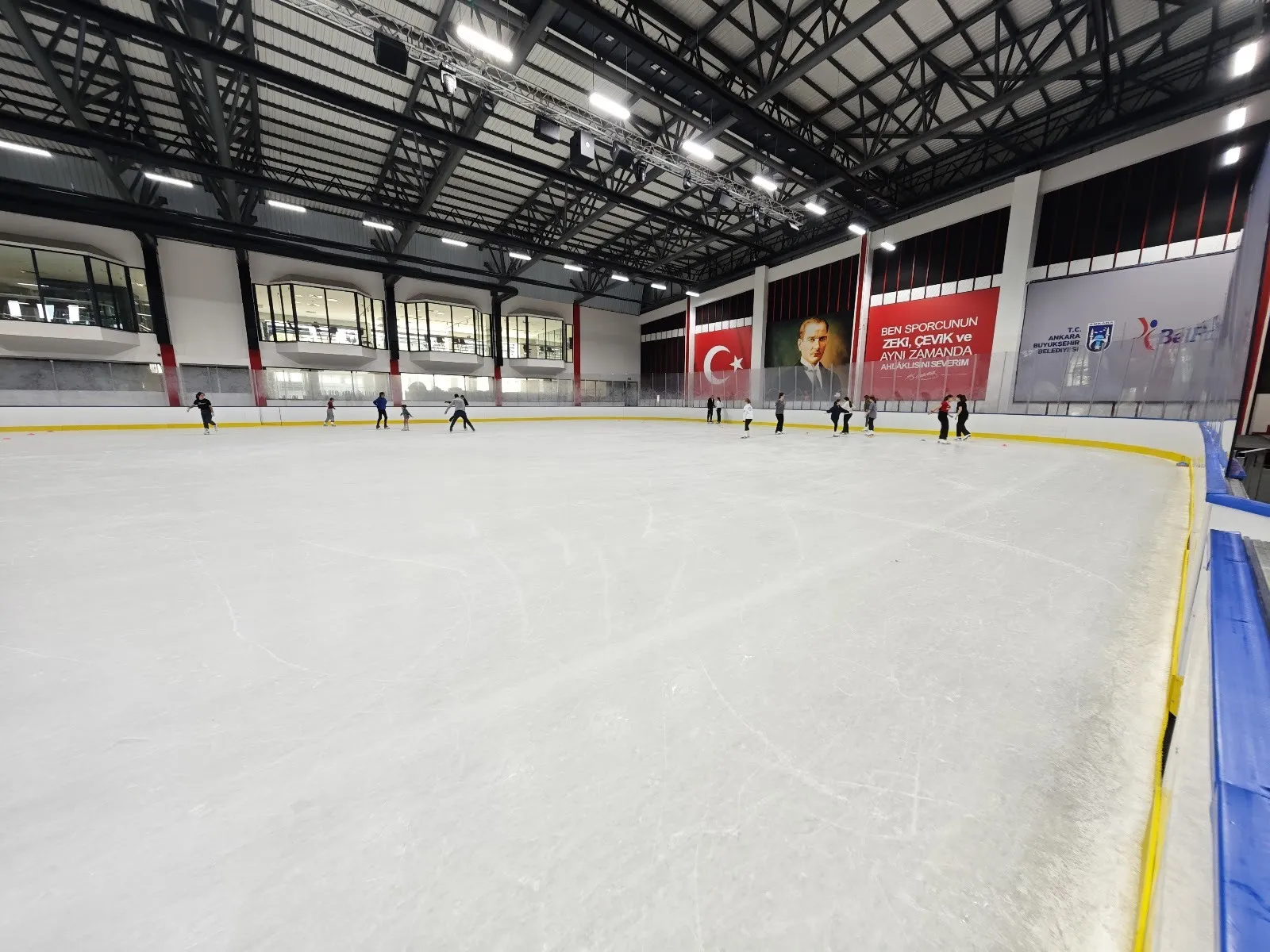 Bülent Ecevit Buz Sporları Salonu'nun buzunda patenciler, arkada tribünler ve çatı kirişleri — Kent Paten (Bülent Ecevit Buz Sporları Salonu) Ankara