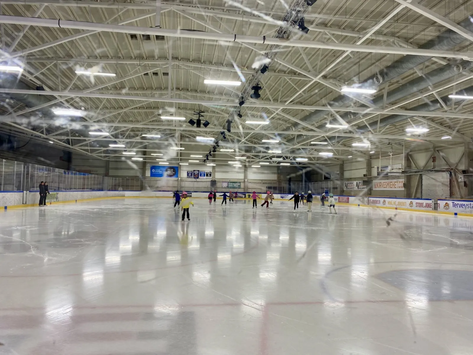 The ice of Keravan Energiahalli under its steel-truss roof during a public skating session, with a few skaters far across the rink — Keravan Energiahalli