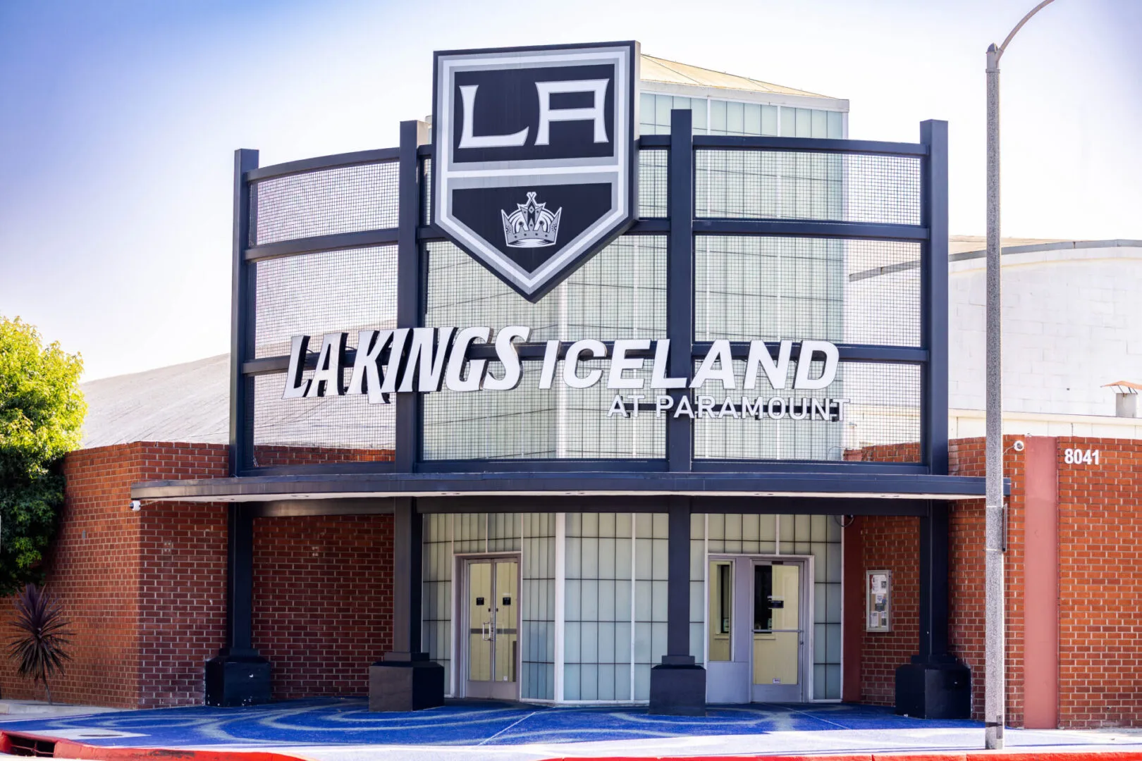 Red-brick entrance under a tall dark steel sign frame carrying the LA Kings shield and LA Kings Iceland at Paramount lettering — LA Kings Iceland