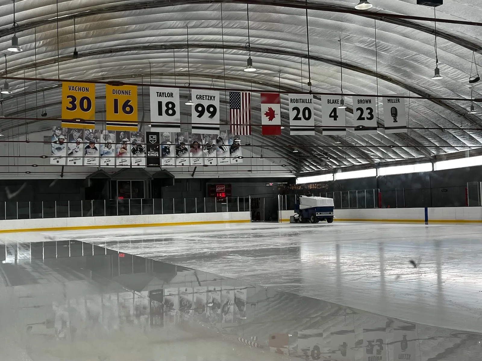 Fresh ice at LA Kings Iceland after resurfacing, under the arched roof hung with retired-number banners and flags — LA Kings Iceland