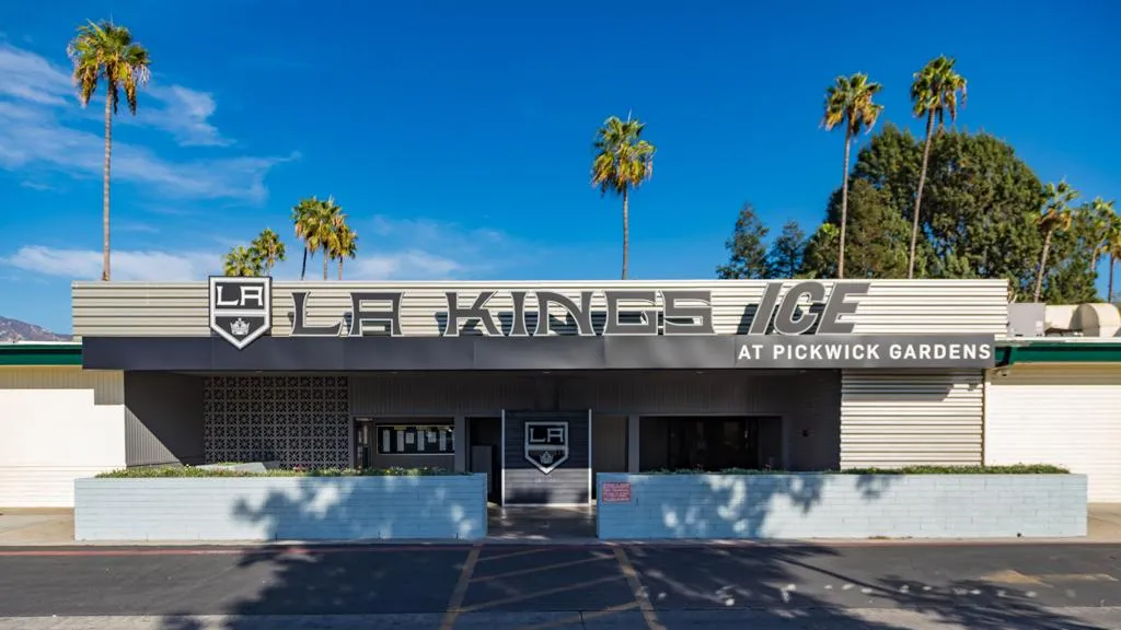 Street-front view of the low mid-century building with a large 'LA KINGS ICE AT PICKWICK GARDENS' sign over the entrance, palm trees behind, under a clear blue sky — LA Kings Ice Pickwick