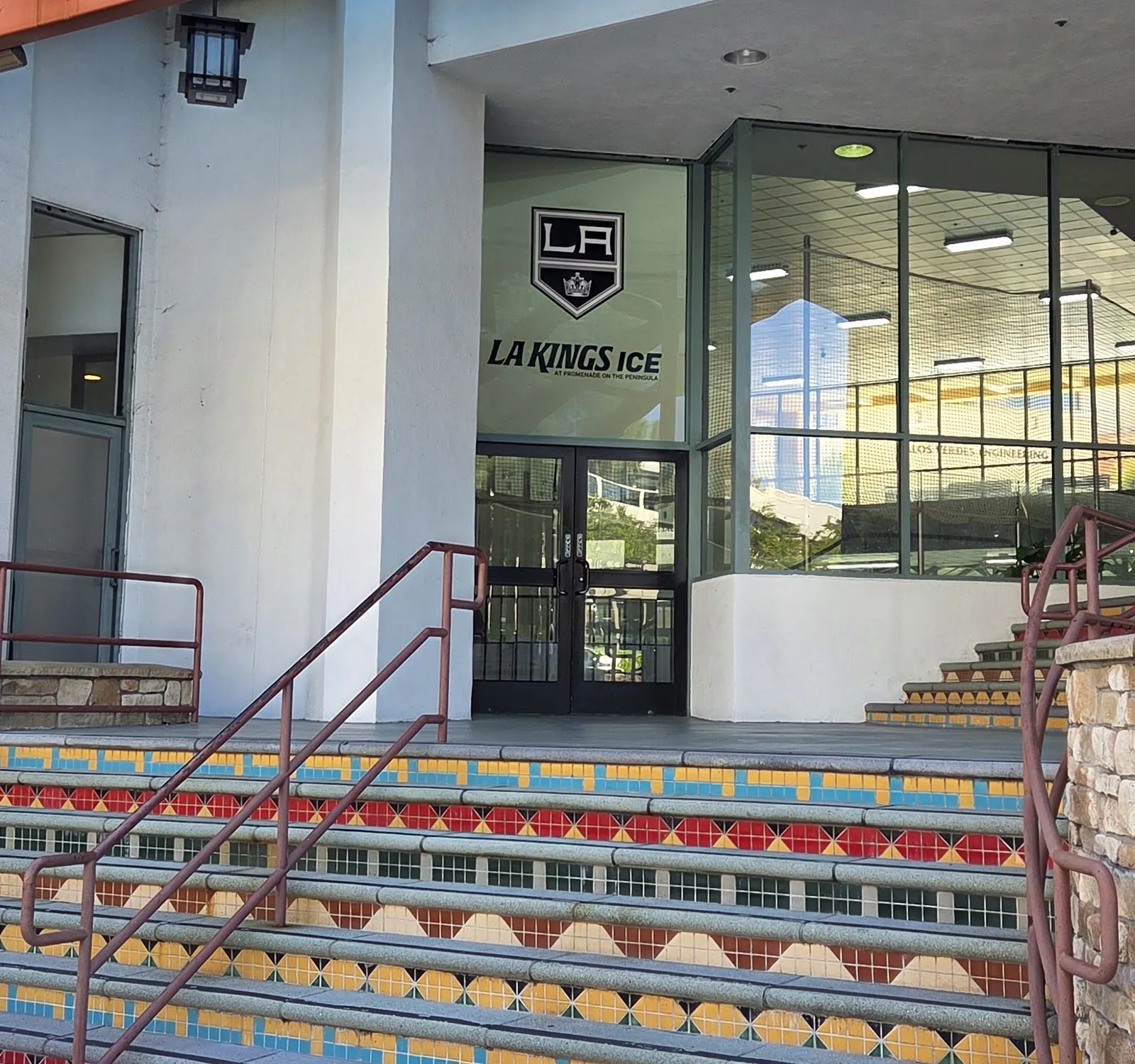La entrada de LA Kings Ice en el Promenade on the Peninsula, con su escudo y su nombre sobre puertas de vidrio en lo alto de unos escalones de azulejo — LA Kings Ice at Promenade on the Peninsula