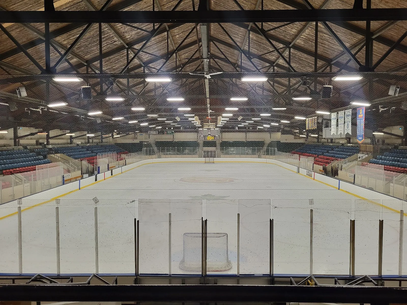 The empty Memorial Centre ice seen from behind one net, under the arena's arched wooden roof with seating along both sides. — Kingston Memorial Centre