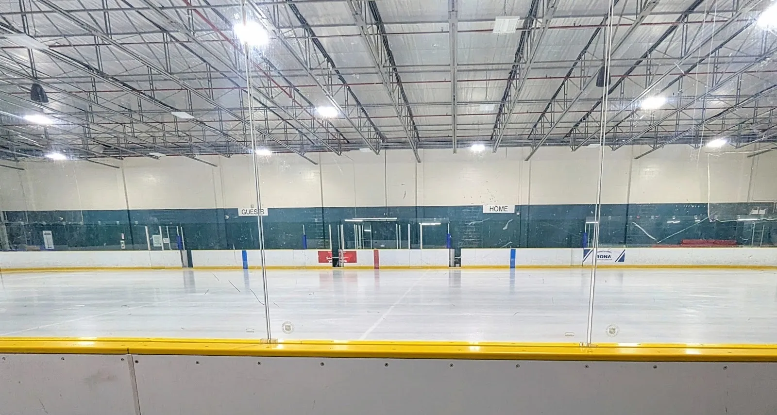 The empty ice at Kinsmen Arena seen from the players' bench, home and guest benches across the sheet under a white steel-truss roof. — Kinsmen Arena (London)
