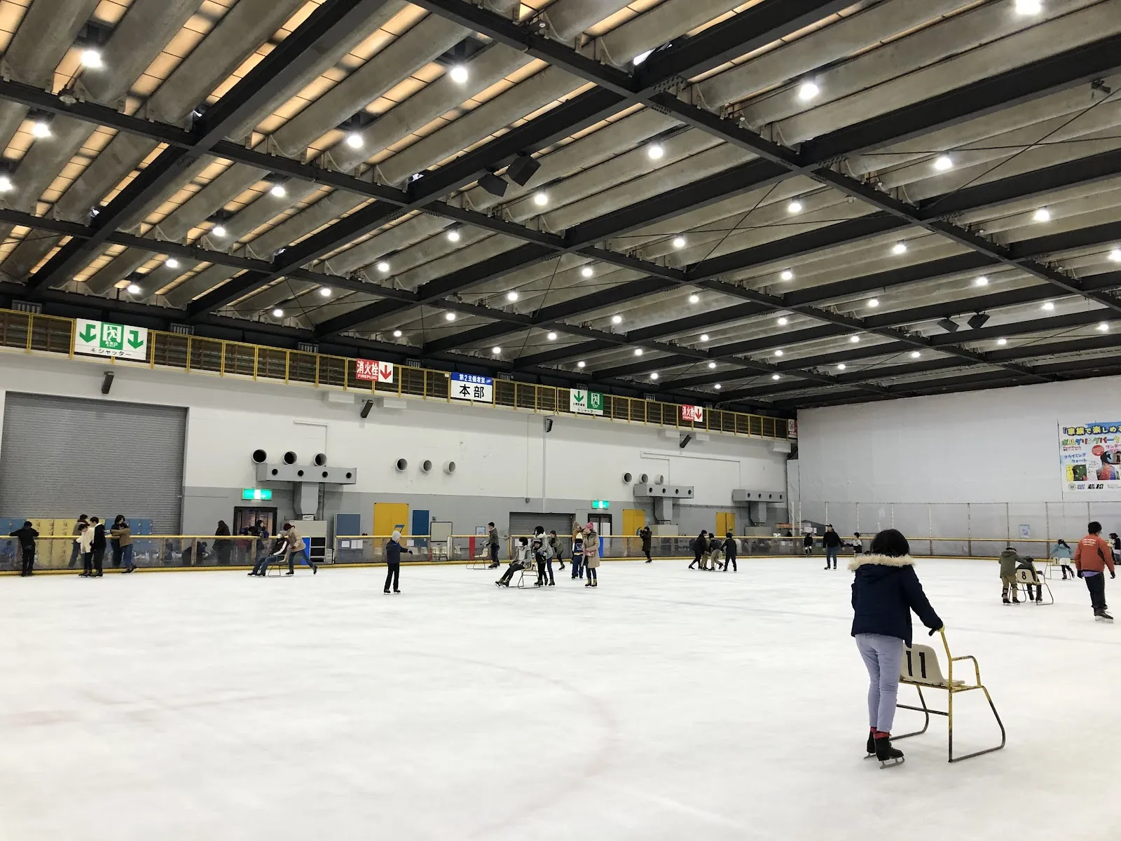 展示場の中にある、北九州アイススケートセンターの30×60メートルのリンク。一般の滑走者が氷面に散らばっています — Kitakyushu Ice Skate Center