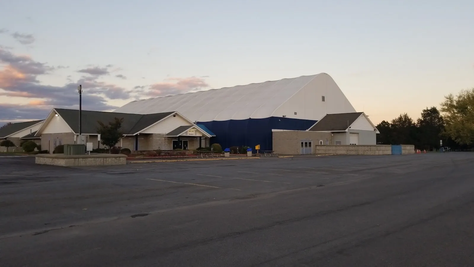 El edificio de Kiwanis Ice Arena con techo de tela y su bloque de entrada al atardecer, visto al otro lado del estacionamiento vacío — Kiwanis Ice Arena