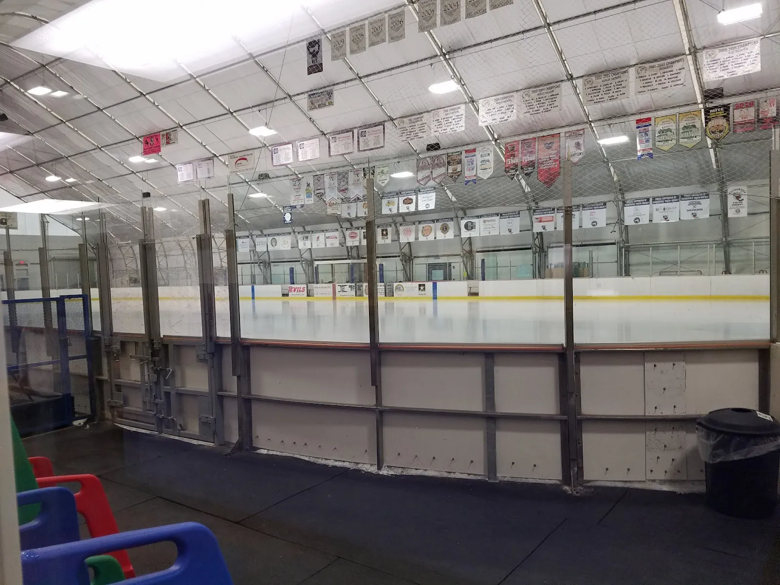 El hielo vacío de Kiwanis Ice Arena visto sobre las vallas y las bancas, con filas de mantas de equipos colgando del techo de tela — Kiwanis Ice Arena