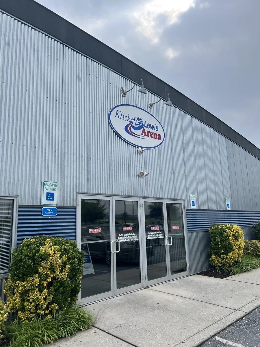 Klick Lewis Arena's glass entrance beneath its oval arena sign. — Klick Lewis Arena