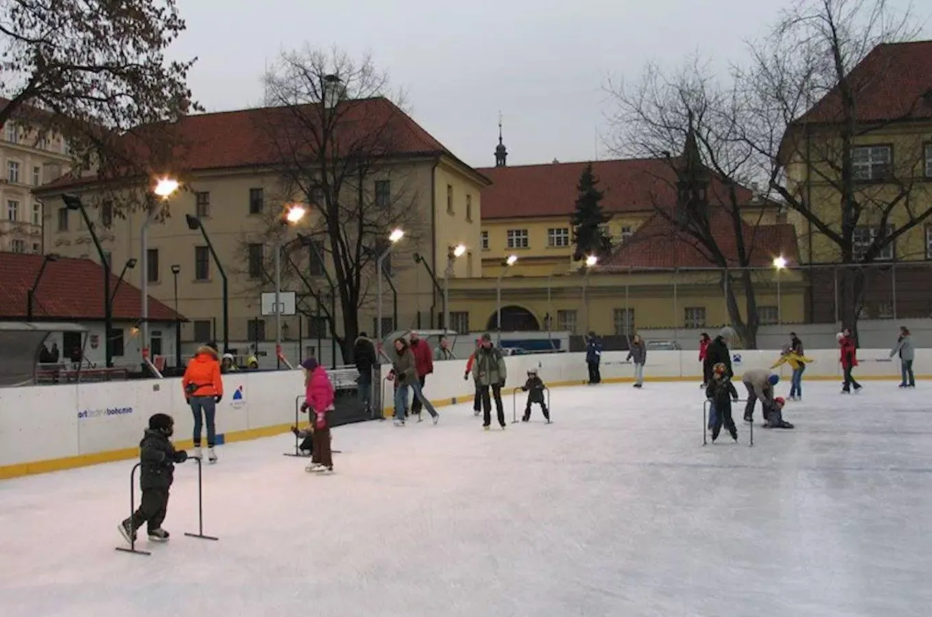 Children and adults skating at the Na Františku rink in Prague 1, with historic buildings and bare trees behind the boards. — Kluziště Na Františku (Praha 1)