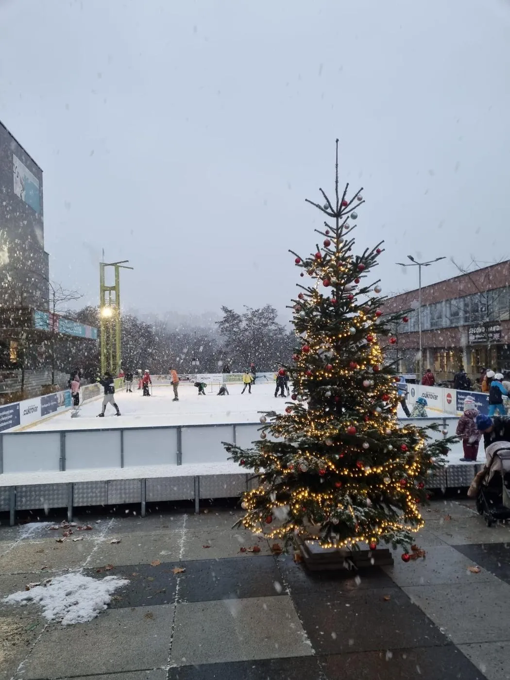 The Sofijské náměstí rink in Prague 12 behind a decorated Christmas tree, with a few skaters on the ice. — Kluziště Sofijské náměstí (Praha 12)
