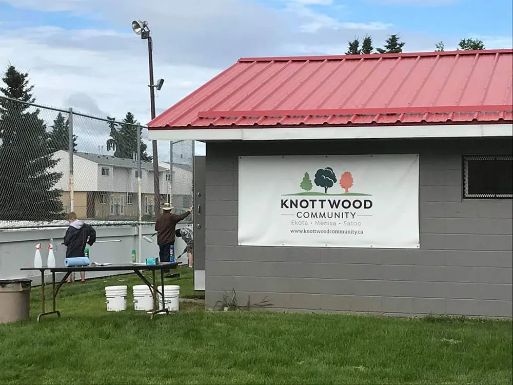 La caseta de la pista de Ekota con el letrero de la comunidad de Knottwood, junto a la pista, con voluntarios trabajando al fondo — Knottwood Community League Rink (Ekota Rink)
