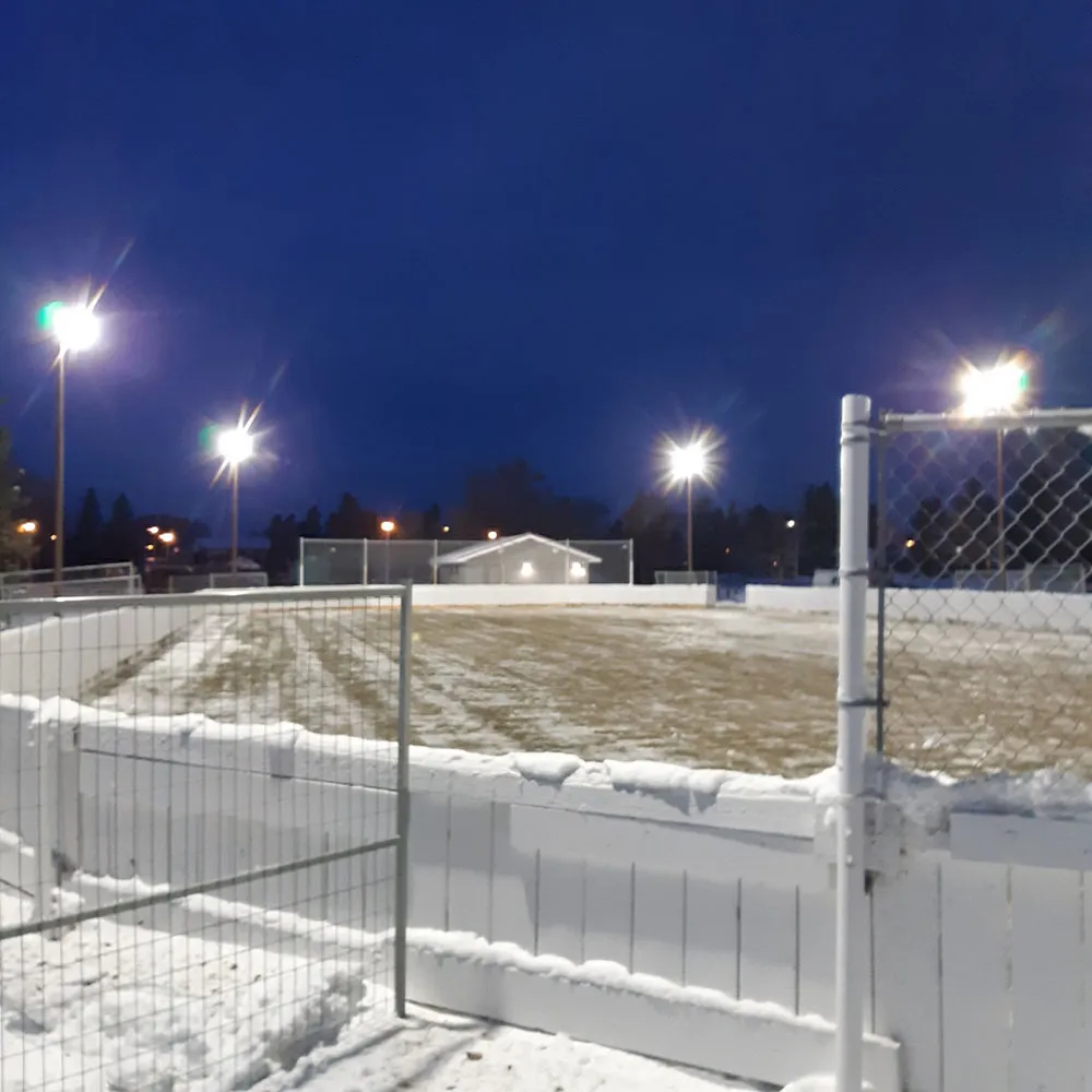La pista de Ekota de noche bajo nuevos reflectores, con vallas blancas y una superficie cubierta de nieve — Knottwood Community League Rink (Ekota Rink)