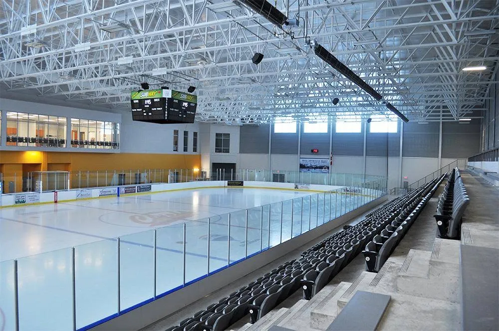 The empty main rink at the Komoka Wellness Centre, seen from the upper seats past the glass, scoreboard hanging under white steel trusses. — Komoka Wellness Centre