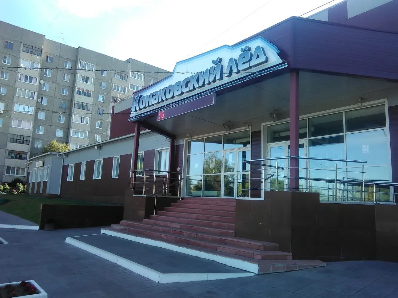 The entrance of the Konakovsky Led ice arena with its lit sign and red-brick steps — Konakovsky Led Ice Arena