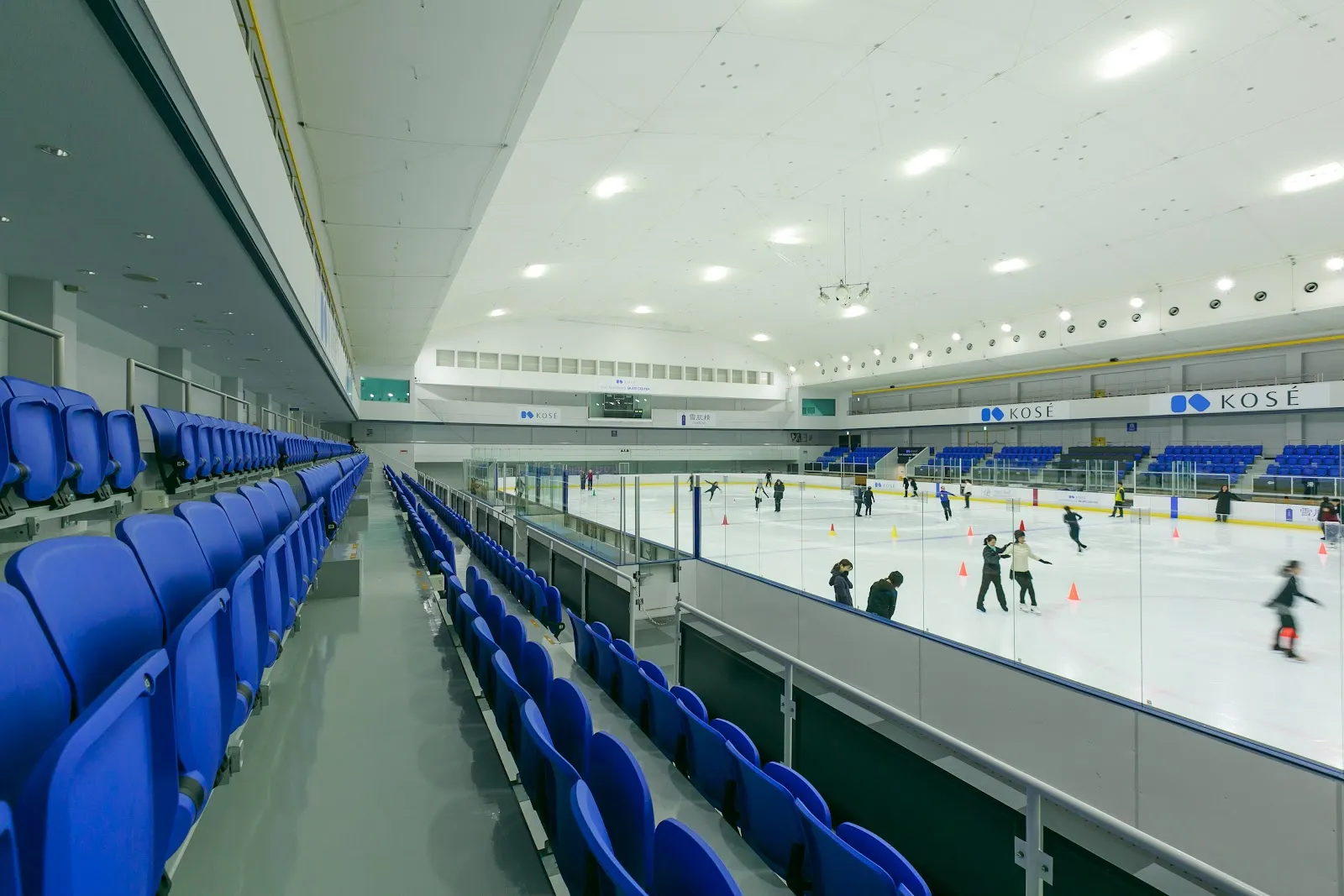 一般滑走中のKOSÉ新横浜スケートセンターの氷面を、青い客席に沿って見たところ — KOSÉ Shin-Yokohama Skate Center