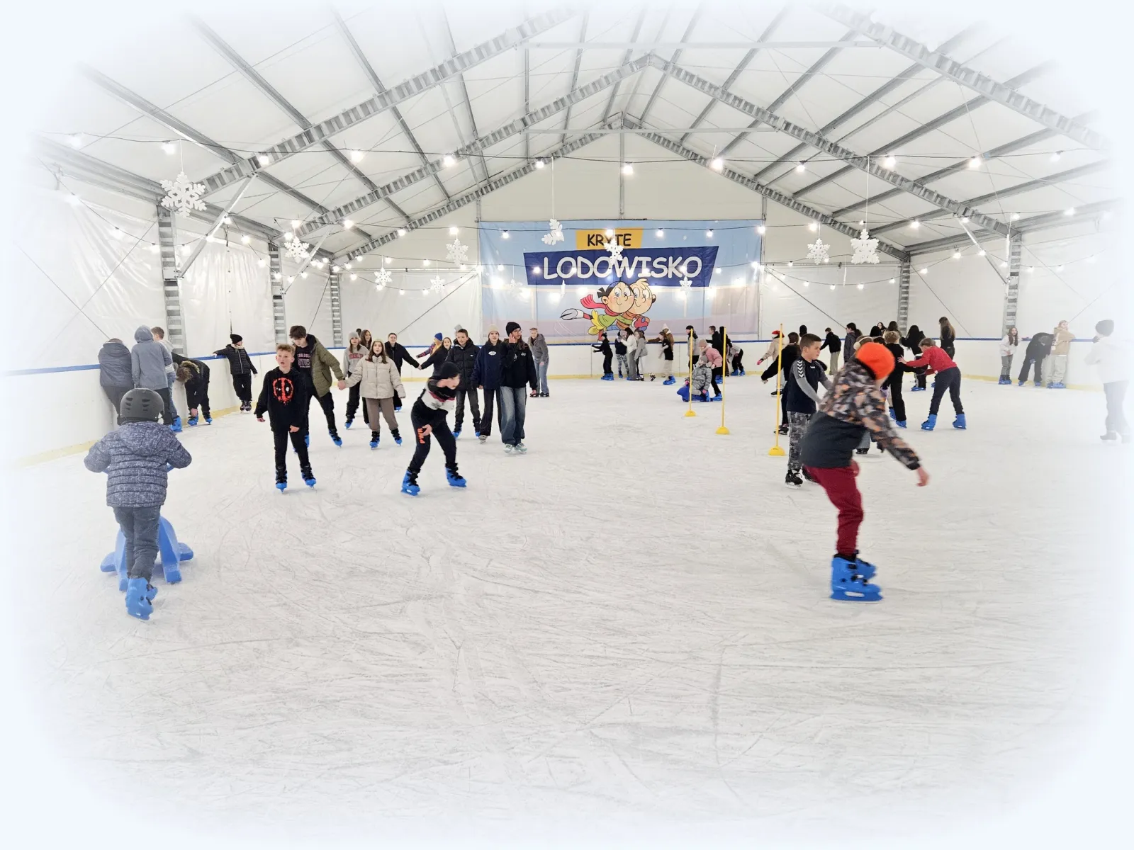 A public skating session under the white tent roof of the Dzierżoniów covered rink, with skaters spread across the ice. — Kryte Lodowisko OSiR Dzierżoniów