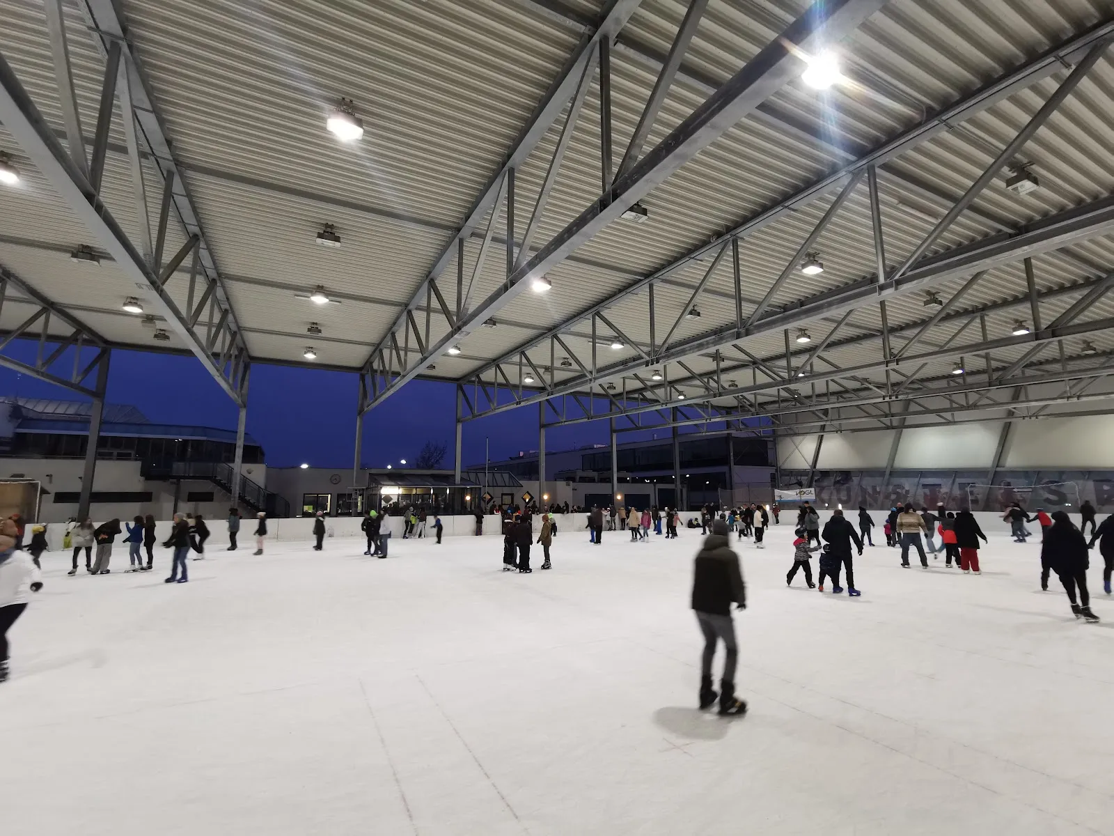 Public skating on the large open-sided ice sheet of the Eisarena Ternitz at dusk under the steel roof — Kunsteisarena Ternitz