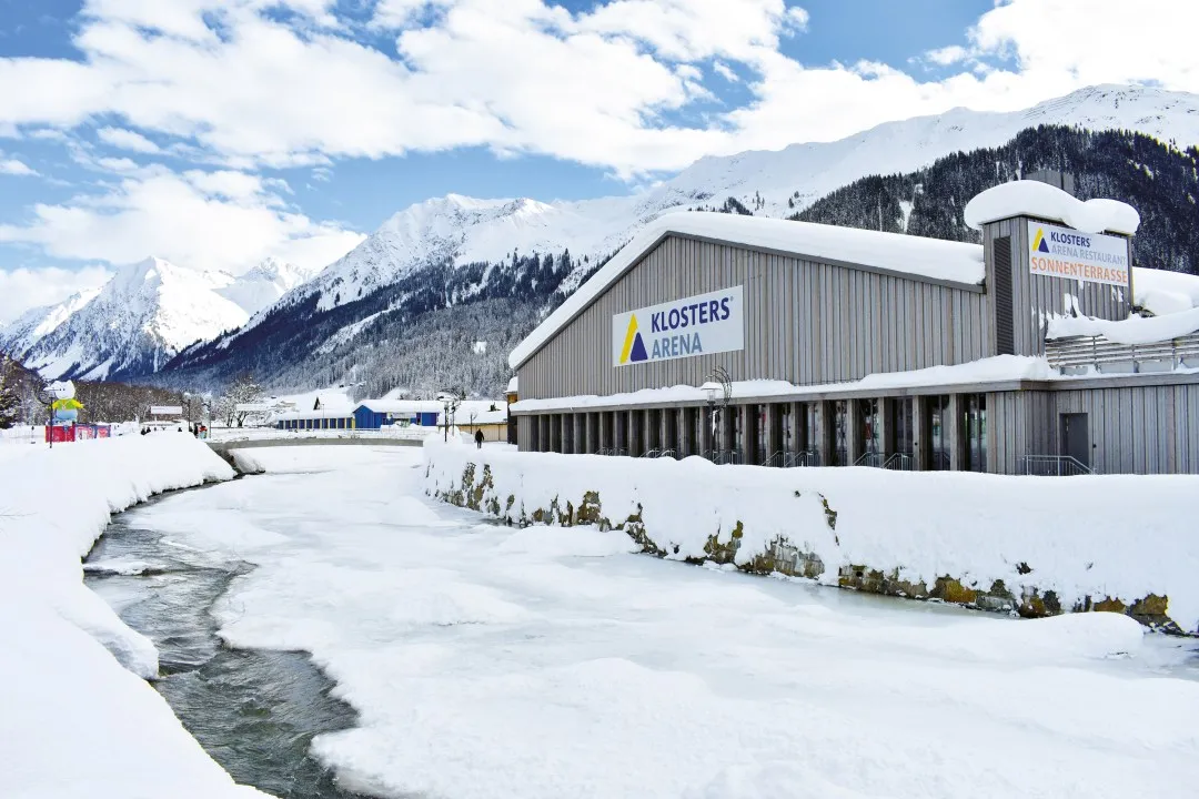 The Arena Klosters building beside the Landquart in winter — Kunsteisbahn Arena Klosters