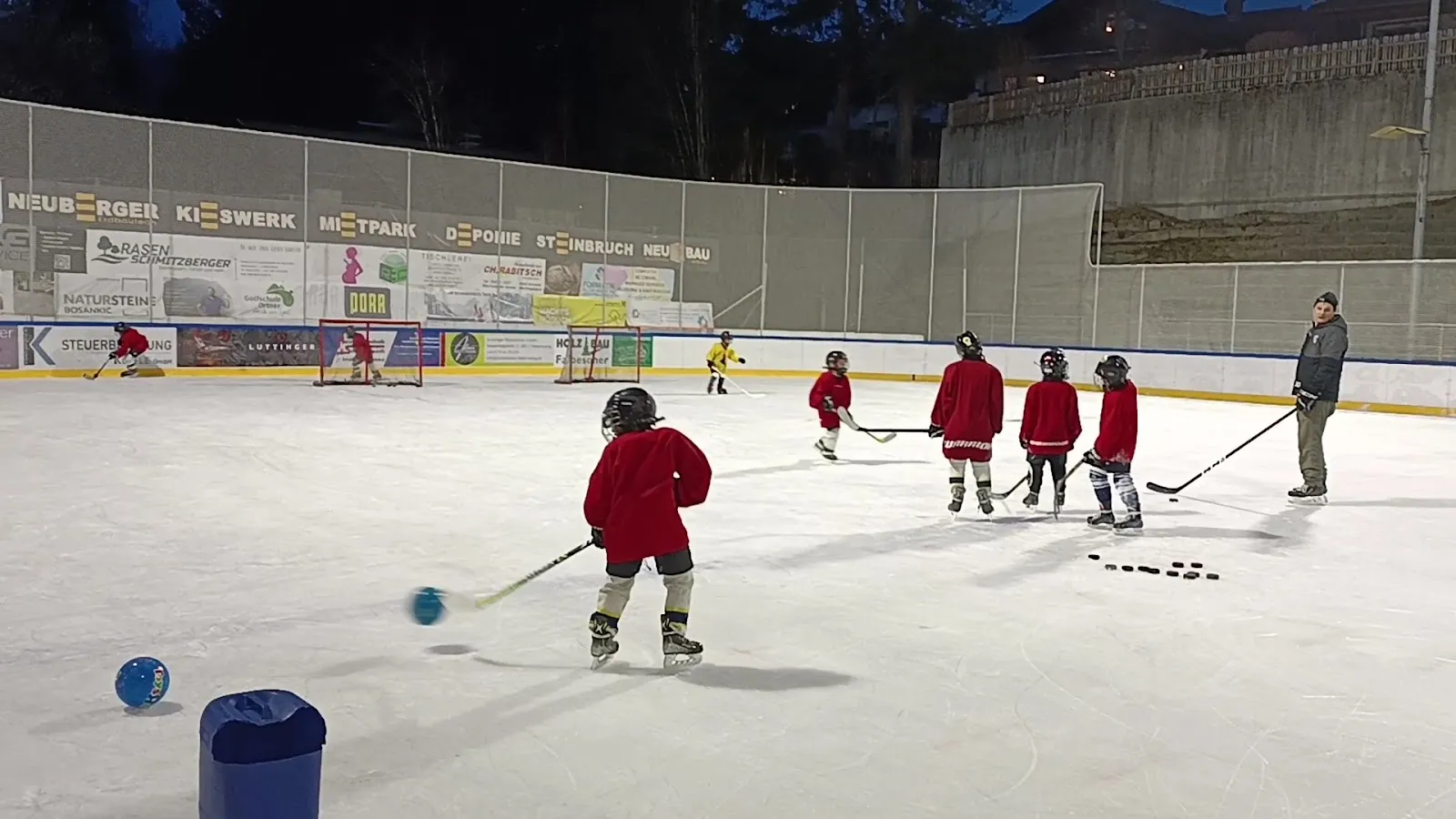 Children practising ice hockey on the open-air ice of the Kunsteisbahn Ehrwald at night, under the floodlit stand. — Kunsteisbahn Ehrwald