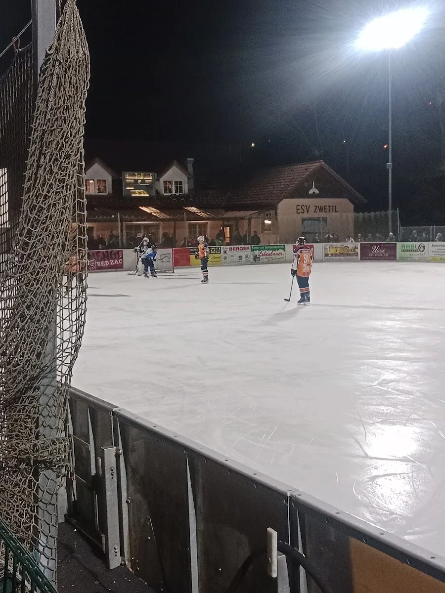 Ice hockey on the floodlit sheet of the Kunsteisbahn ESV Zwettl at night, with the clubhouse behind the boards — Kunsteisbahn ESV Zwettl