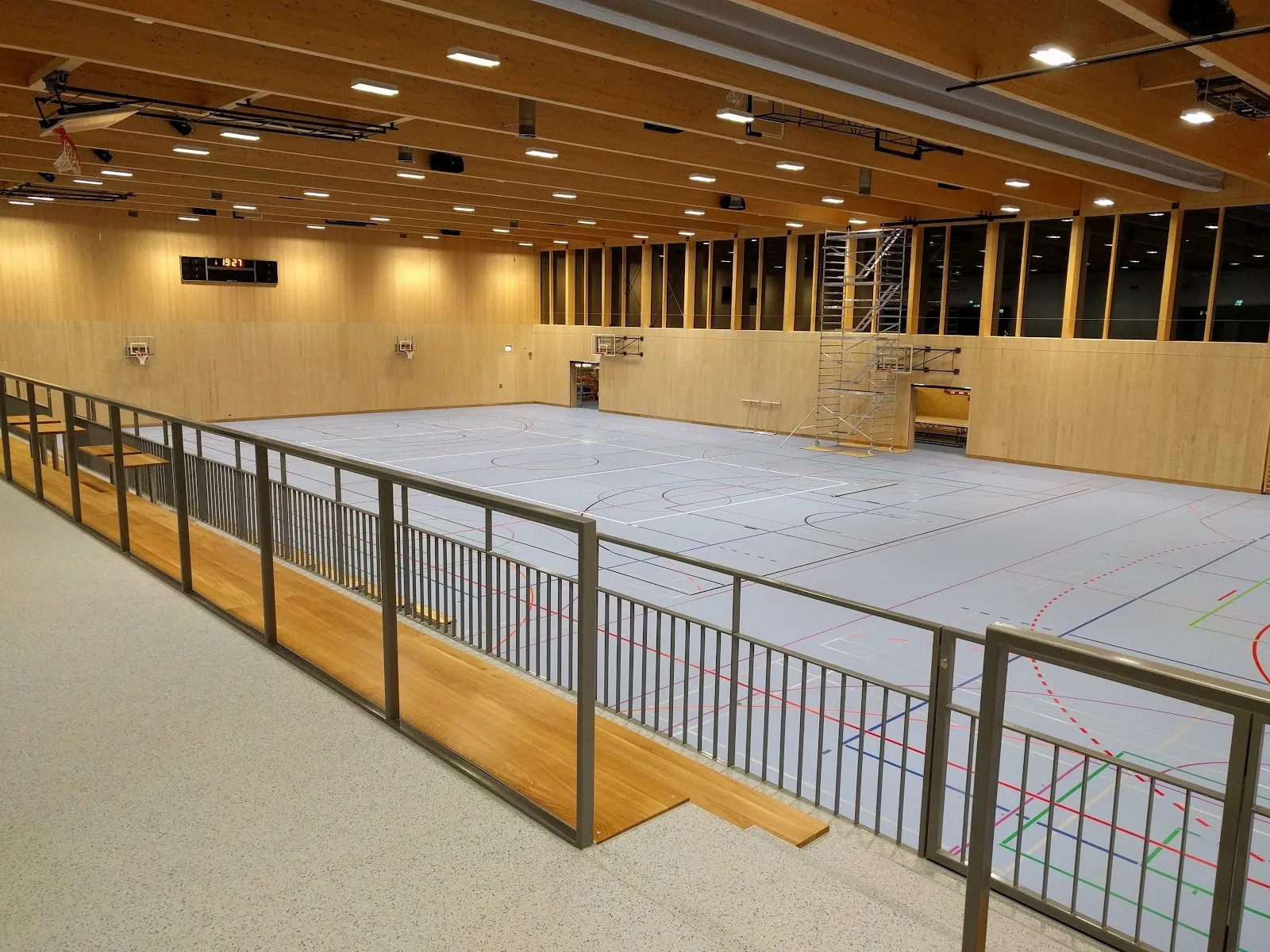 The empty ice sheet of the Kunsteisbahn Hirslen in Bülach seen from the rink-side railing under the timber roof. — Kunsteisbahn Hirslen