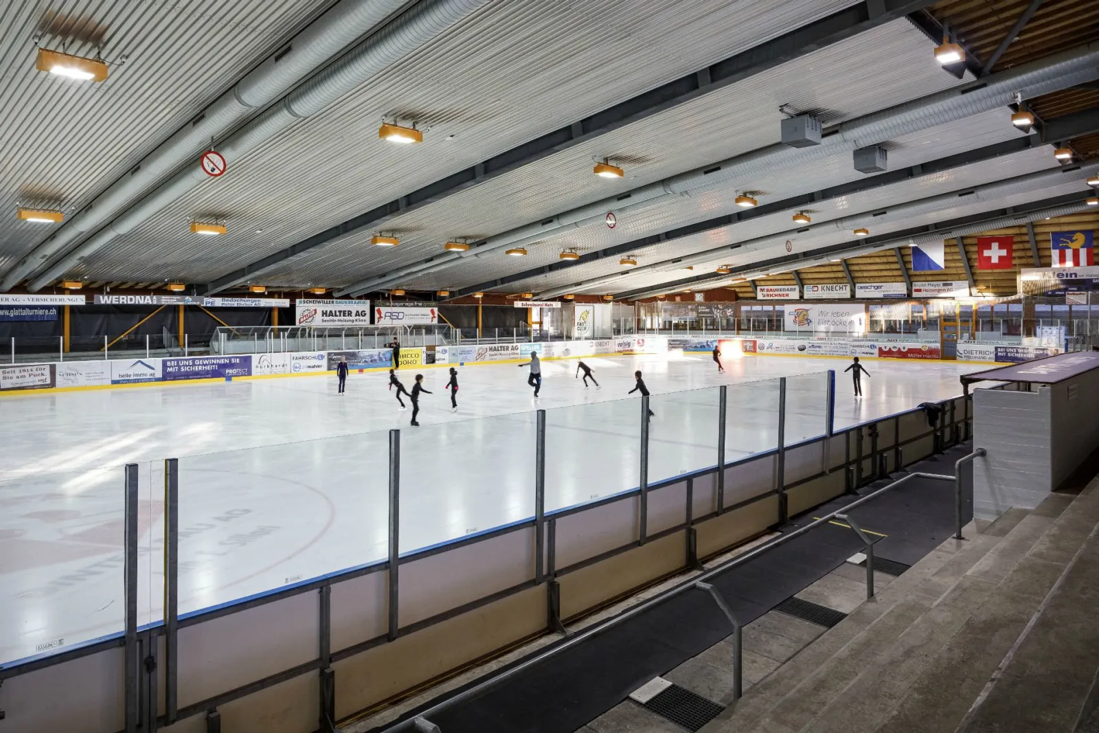 Figure skaters training on the ice of the roofed hall of the Kunsteisbahn Im Chreis in Dübendorf, seen from the stands — Kunsteisbahn Im Chreis