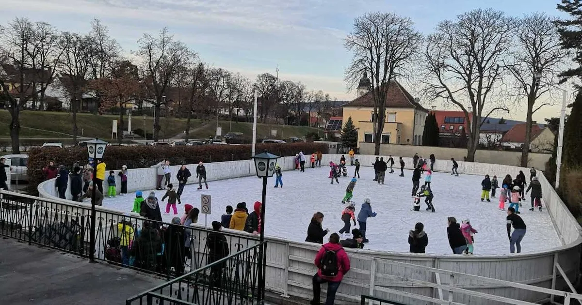 Skaters on the open-air Kunsteisbahn Retz with trees and town buildings behind the ice – Kunsteisbahn Retz