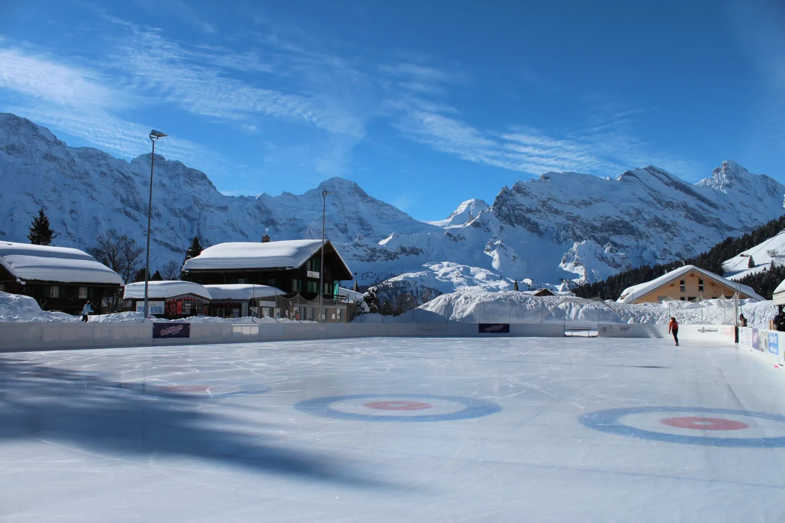 The empty ice field with curling circles and the Mürren mountains behind — Kunsteisbahn Alpines Sportzentrum Mürren