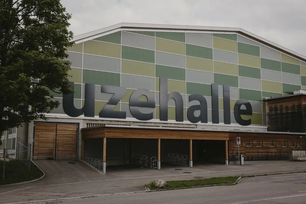 Die Uzehalle in Niederuzwil mit ihrer grün-grauen Fassade und dem überdachten Eingang – Kunsteisbahn Uzehalle