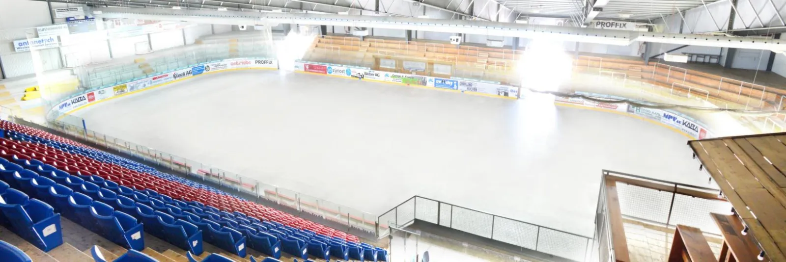 The empty ice surface of the Kunsteisbahn Wetzikon seen from the stands, with the boards and the grandstand seats — Kunsteisbahn Wetzikon