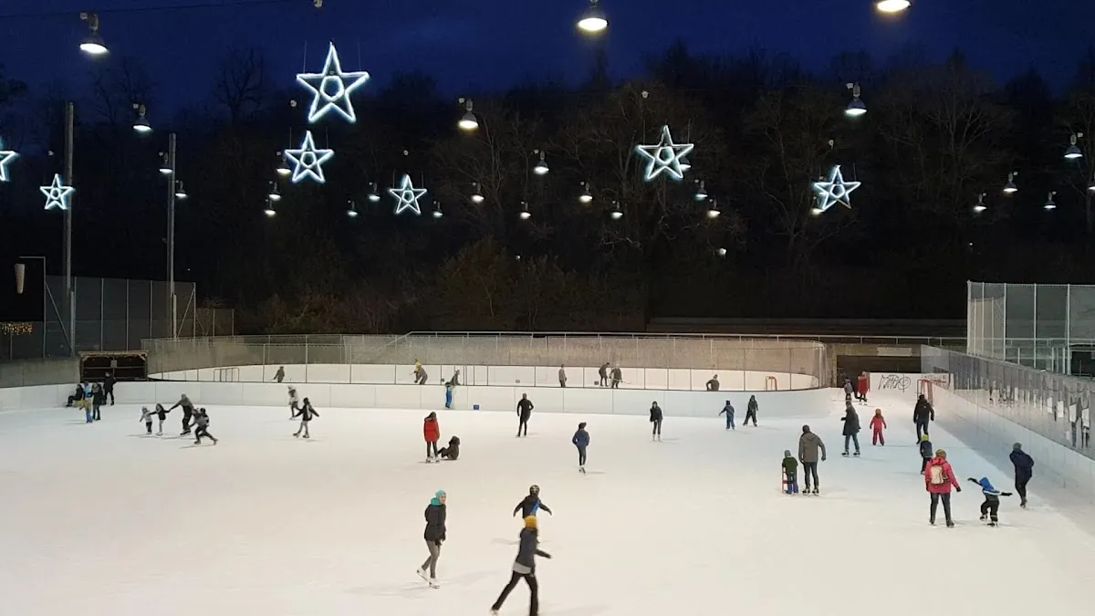 Das Freiluft-Eis der Kunsteisbahn Weyermannshaus in Bern an einem Winterabend, beleuchtet von sternförmigen Dekorationen, mit Eisläuferinnen und Eisläufern, die sich über die Fläche verteilen – Kunsteisbahn Weyermannshaus