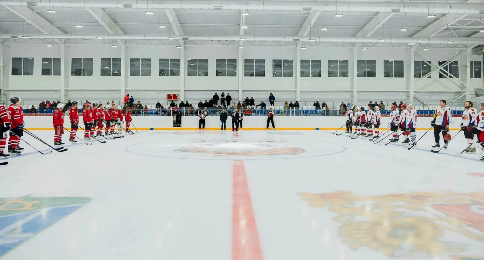 Two youth hockey teams lined up on the blue lines of the Kutergin Ice Centre rink before a game, with spectators along the boards — Kutergin Ice Centre Sysert
