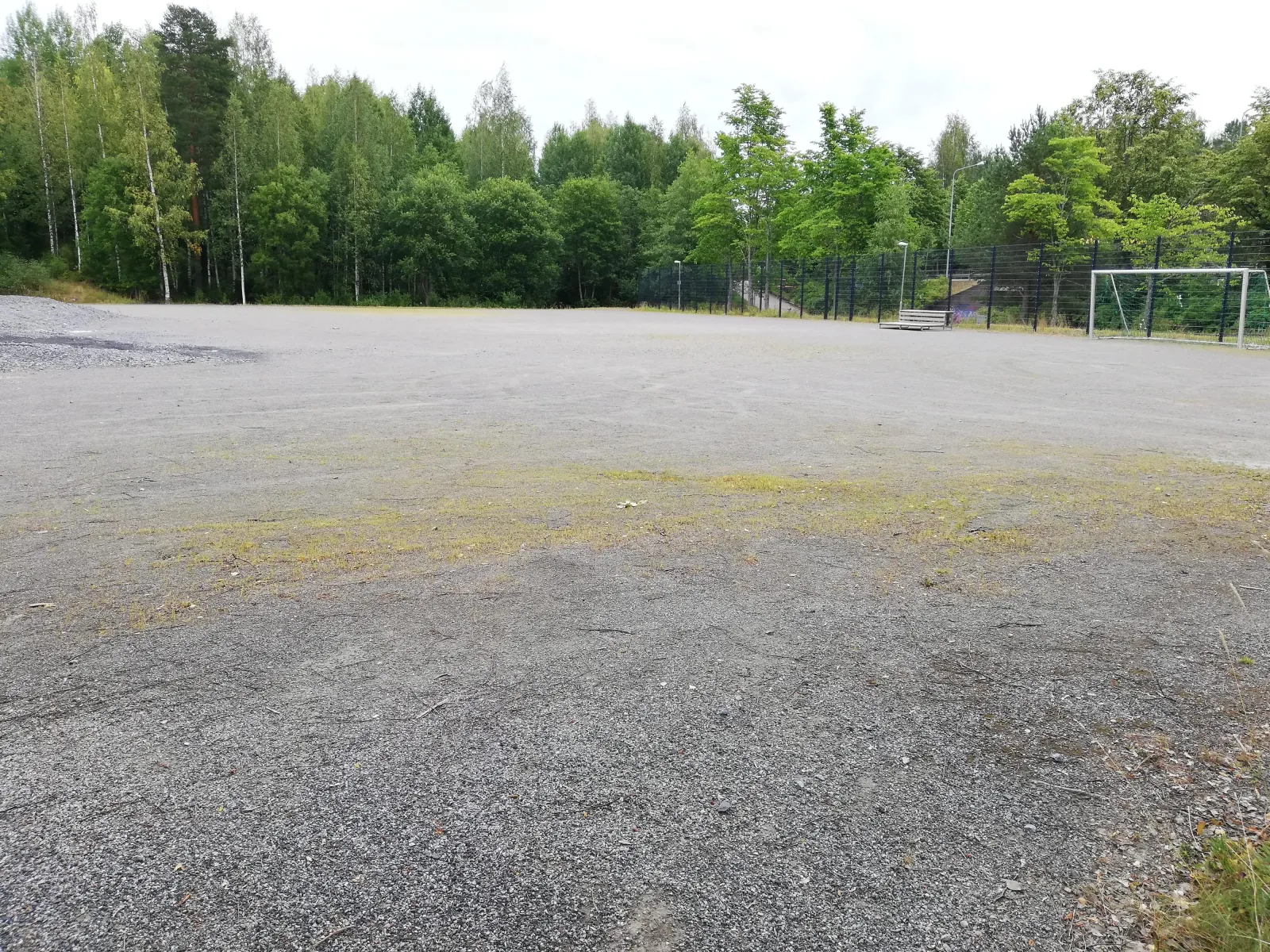 The gravel field at Kuvelampi in Kuopio, which serves as a skating field in winter, seen in summer with birch woods and a goal in the distance. — Kuvelammen luistelukenttä