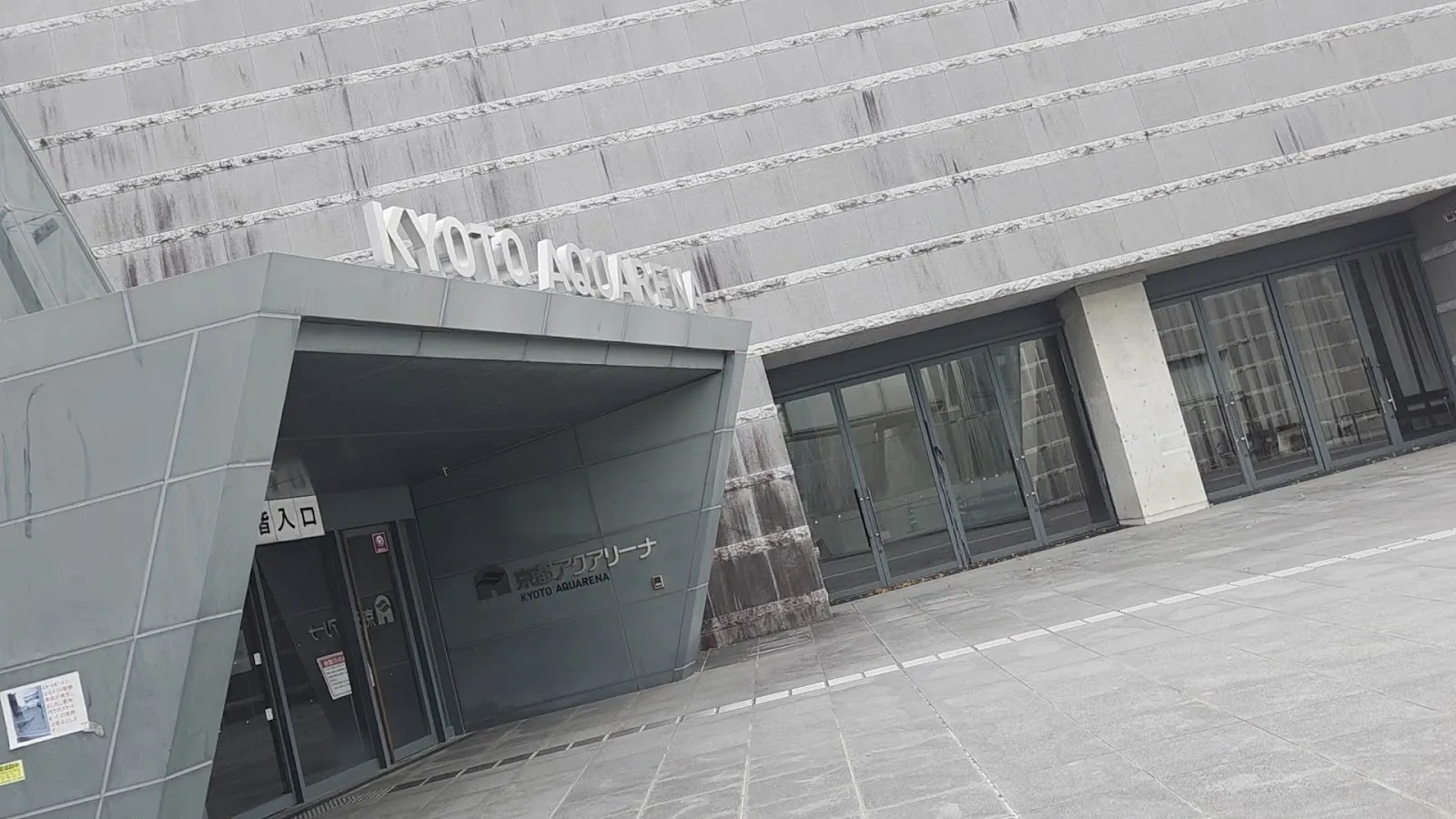 The grey concrete entrance of Kyoto Aquarena with its name in steel letters above the doorway. — Kyoto Aquarena