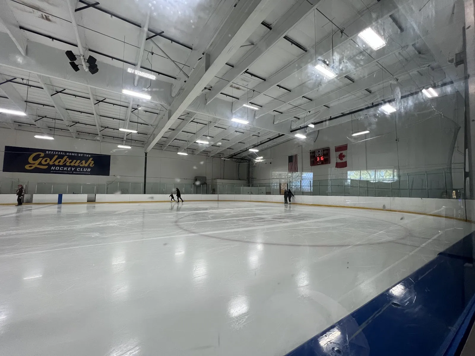 The sheet under a white steel roof, with a Goldrush Hockey Club banner on the far wall and a few skaters at the end. — Lake Forest Ice Palace