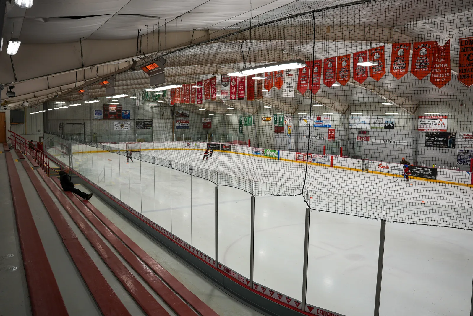 The ice from the red bench seating, with red banners hung along the roof trusses. — Lakefield-Smith Community Centre