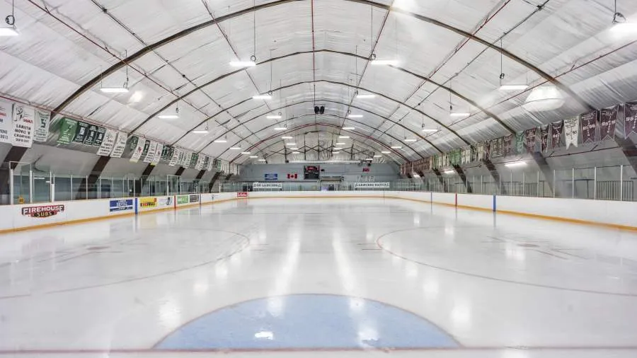 El hielo vacío de Lambeth bajo el techo en arco, con estandartes de equipos a ambos lados y anuncios de patrocinadores en las vallas. — Lambeth Arena